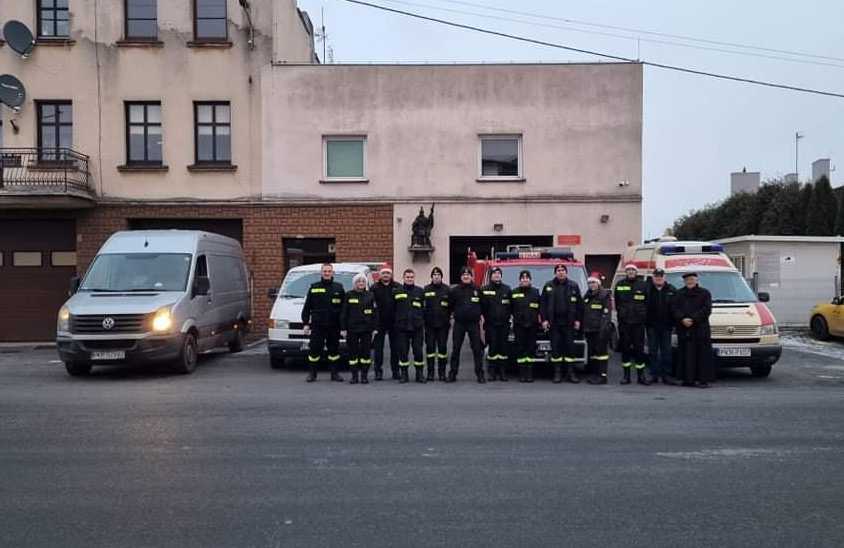 Zdjęcie grupowe, na pierwszym planie strażacy, którzy rozwozili dary, dalej samochody oraz budynek remizy OSP Koźmin Wlkp.
