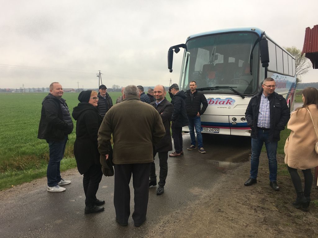 Grupa kobiet i mężczyzn stoi przed autobusem.