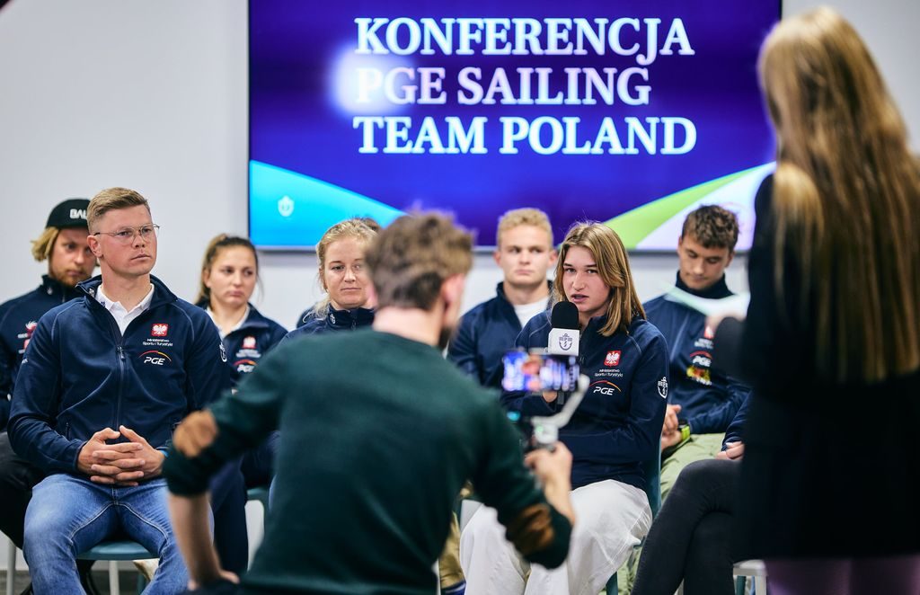 Konferencja prasowa, uczestnicy siedza na kzesłach, julia mówi do mikrofomu.