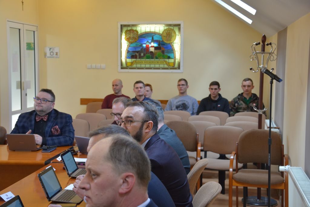 Obrady radnych. Radni siędzą za stołem.