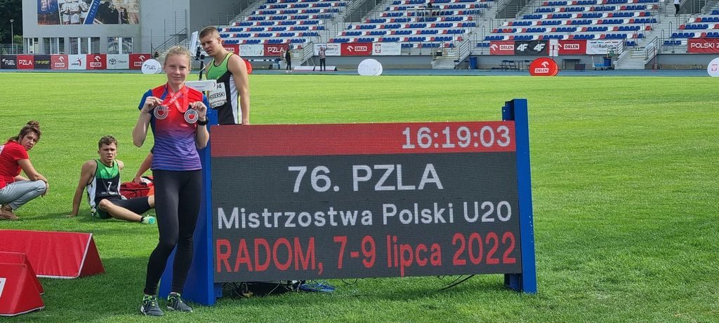 Zawodniczka prezentuje medale na tle stadionu.