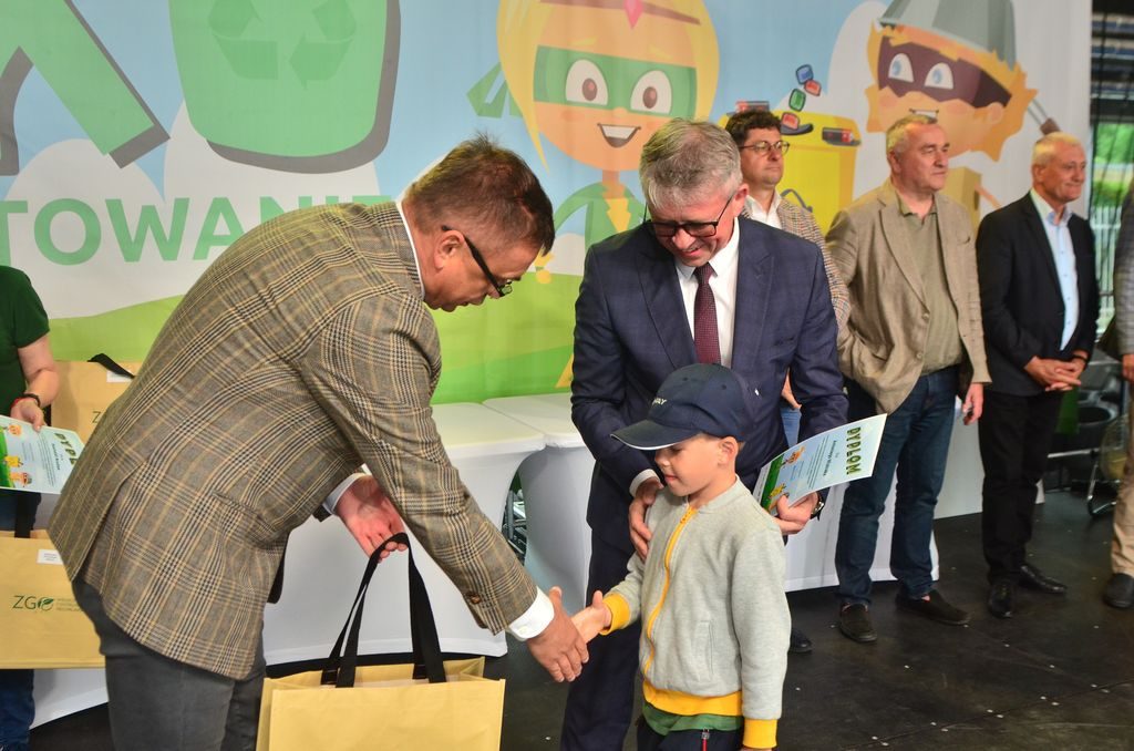 Na scenie mężczyzna wręcza nagrodę i gratuluje dziecku.