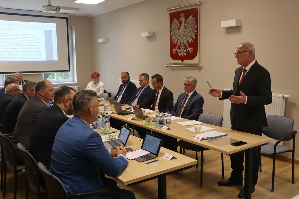 Radni siedzą za stołem, burmistrz stoi i mówi.